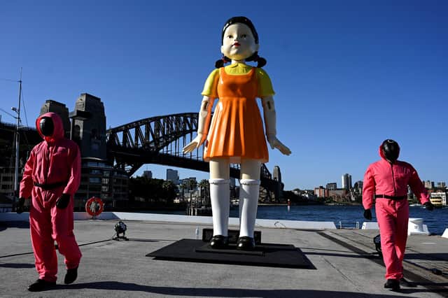 Cosplayers stand next to a 4.5 metre tall replica doll from the Netflix series “Squid Game” on display at the harbour in Sydney(Photo by SAEED KHAN/AFP via Getty Images)