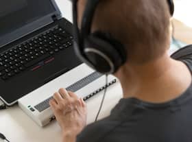Global Accessibility Awareness Day focuses on digital access and inclusion for people with disabilities or impairments. (Image shows visually impaired person working on computer with assistive technology) 