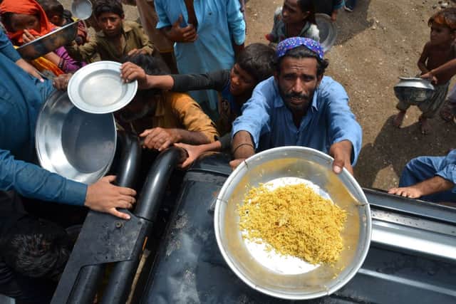 People displaced due to flooding hold pots as they queue receive food in Dera Allah Yar town after heavy monsoon rains in Jaffarabad district, Balochistan province, on August 30, 2022. (Photo by FIDA HUSSAIN/AFP via Getty Images)