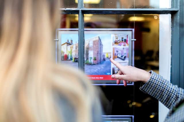 Couple looking and pointing at a property advert in the window of an estate agents or real estate shop window in England in the UK