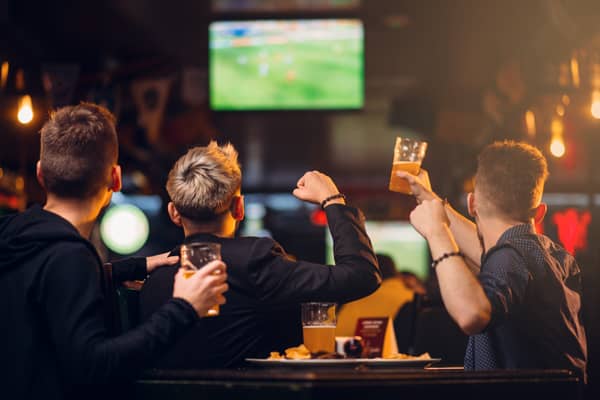 Three men watches football on TV in a sport bar (stock image)