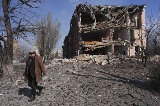 A woman walks past building damaged by shelling in Mariupol, Ukraine, Sunday, March 13, 2022. The surrounded southern city of Mariupol, where the war has produced some of the greatest human suffering, remained cut off despite earlier talks on creating aid or evacuation convoys. (AP Photo/Evgeniy Maloletka)