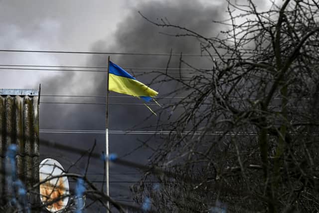 An Ukrainian flag waves in front of smoke rising from a bombed warehouse in the town of Stoyanka, west of Kyiv, on March 4, 2022. - The UN Human Rights Council on March 4, 2022, overwhelmingly voted to create a top-level investigation into violations committed following Russia's invasion of Ukraine. More than 1.2 million people have fled Ukraine into neighbouring countries since Russia launched its full-scale invasion on February 24, United Nations figures showed on March 4, 2022. (Photo by ARIS MESSINIS / AFP) (Photo by ARIS MESSINIS/AFP via Getty Images)